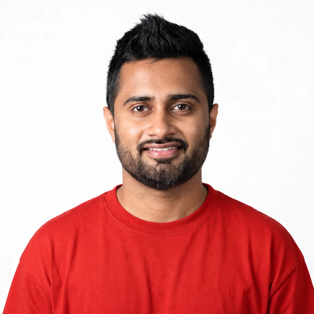Senith B, smiling, in a red t-shirt against a pale studio backdrop.